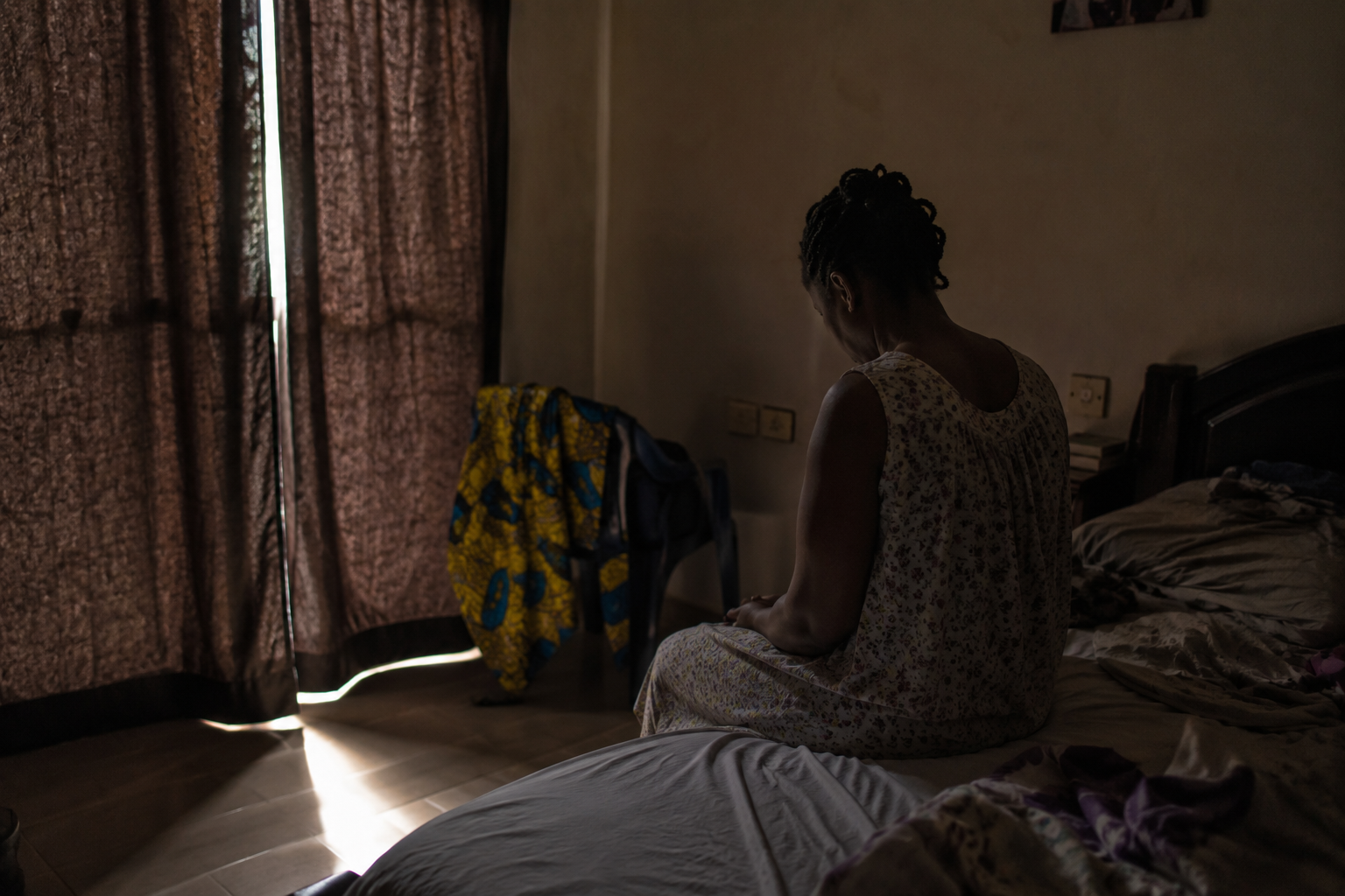 Woman sitting quietly on the edge of a bed, emotionally drained